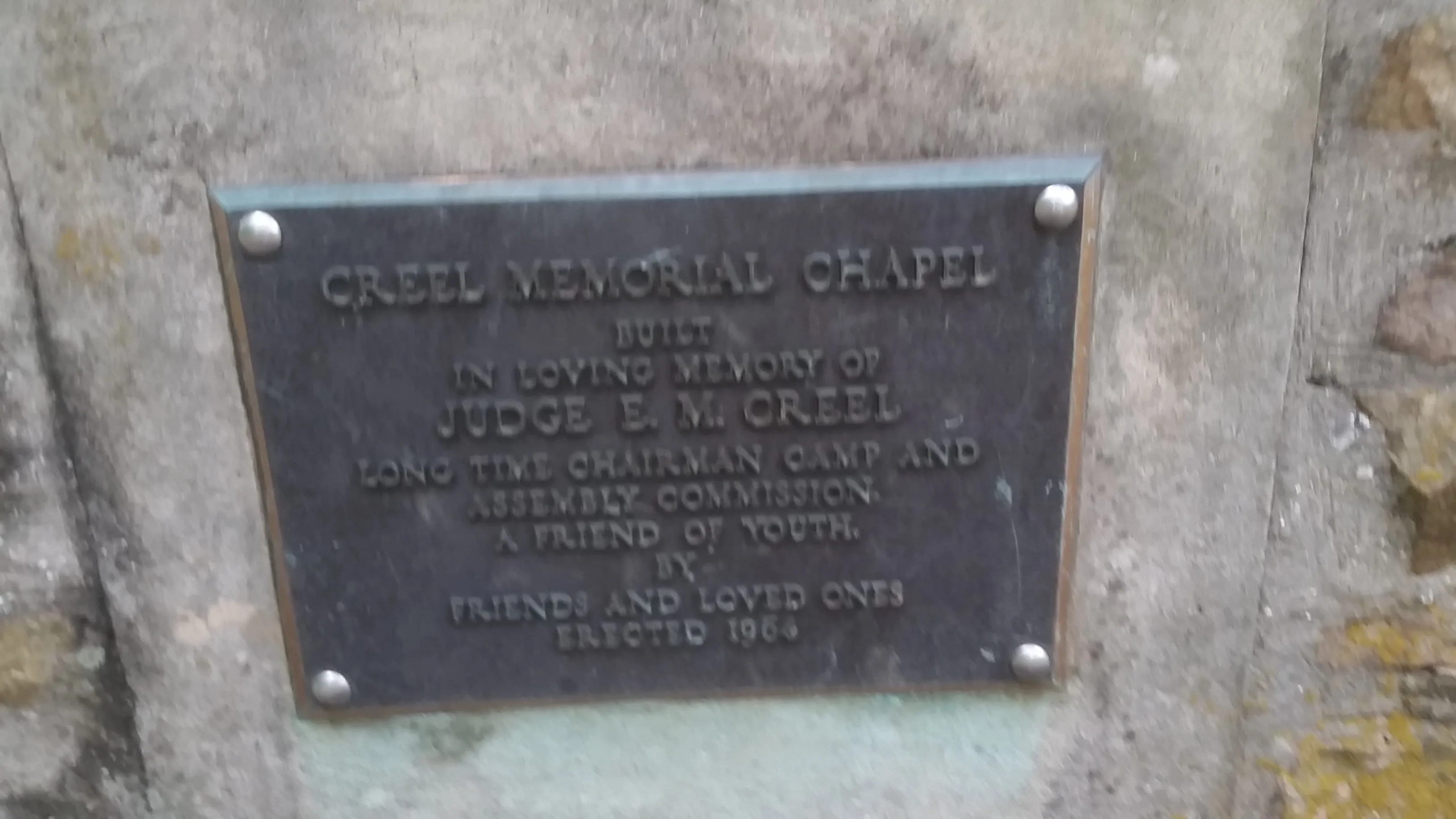Weathered bronze plaque reading Creel Memorial Chapel, in loving memory of Judge E. M. Creel, long time chairman of the Camp and Assembly Commission, a friend of youth, erected 1984