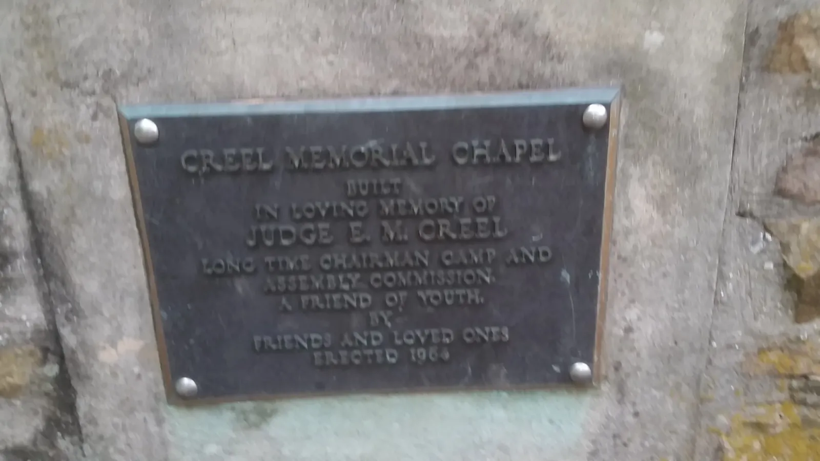 Weathered bronze plaque reading Creel Memorial Chapel, in loving memory of Judge E. M. Creel, long time chairman of the Camp and Assembly Commission, a friend of youth, erected 1984