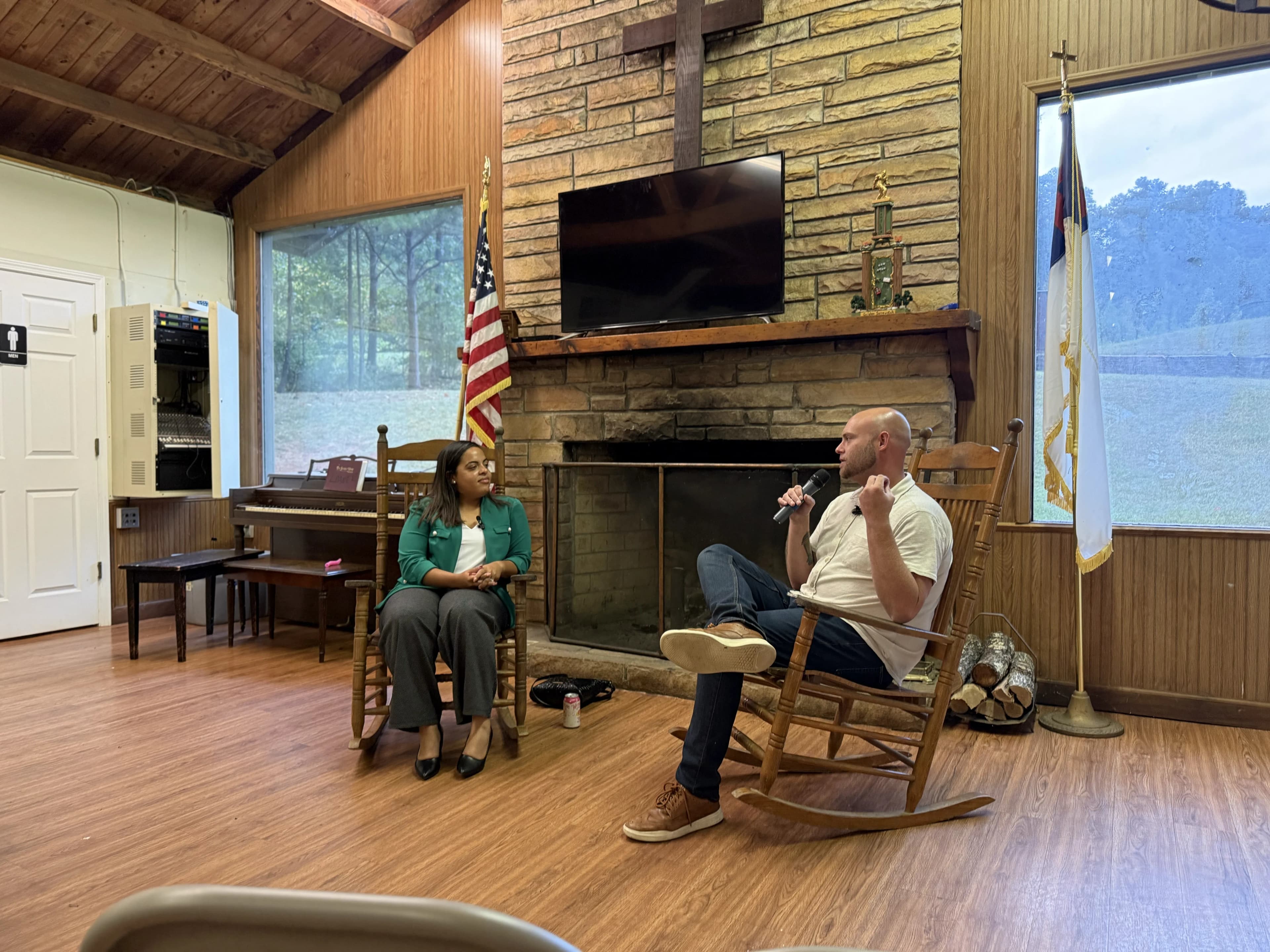 Ciara Smith-Roston being interviewed by Kyle at Camp Lee, the two seated in rocking chairs by a stone fireplace