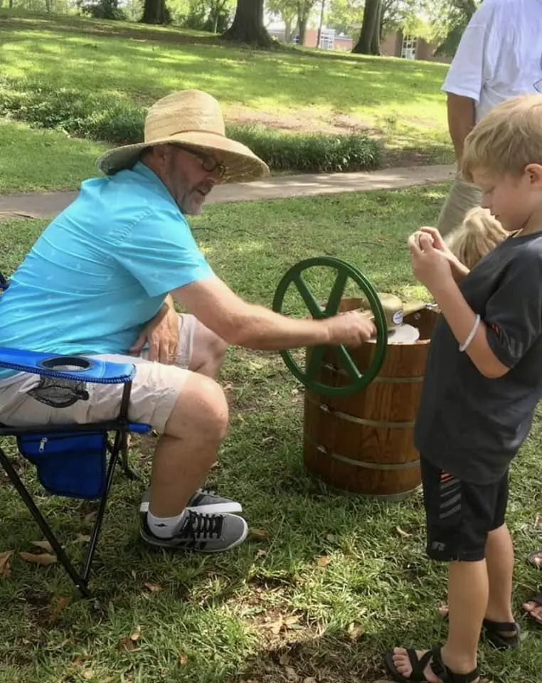Jay Jenkins in a straw hat hand-churning ice cream with a young child at a community event