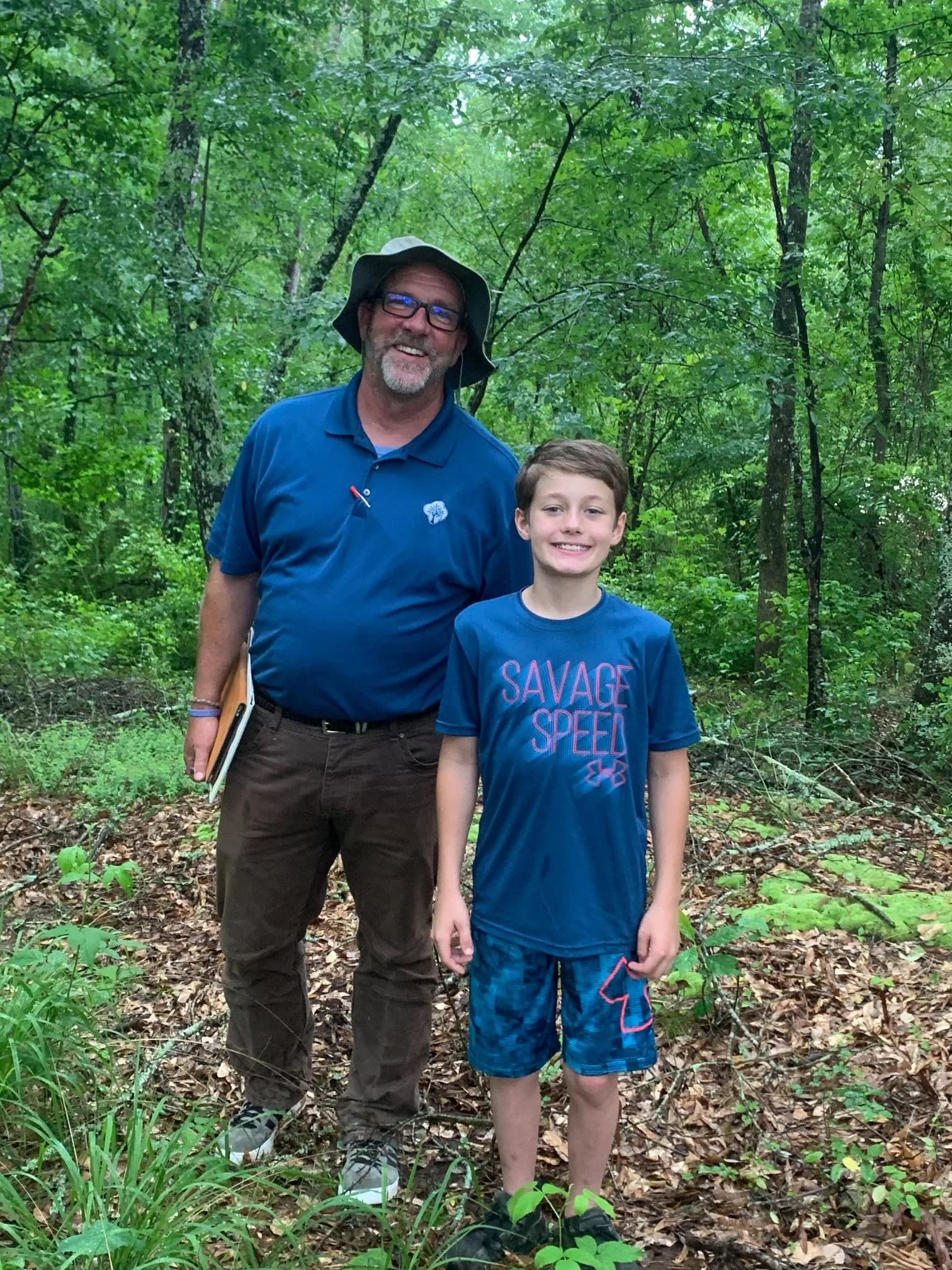 Jay Jenkins standing in the woods with Wish Kid Rylan during a site visit for the Make-A-Wish treehouse