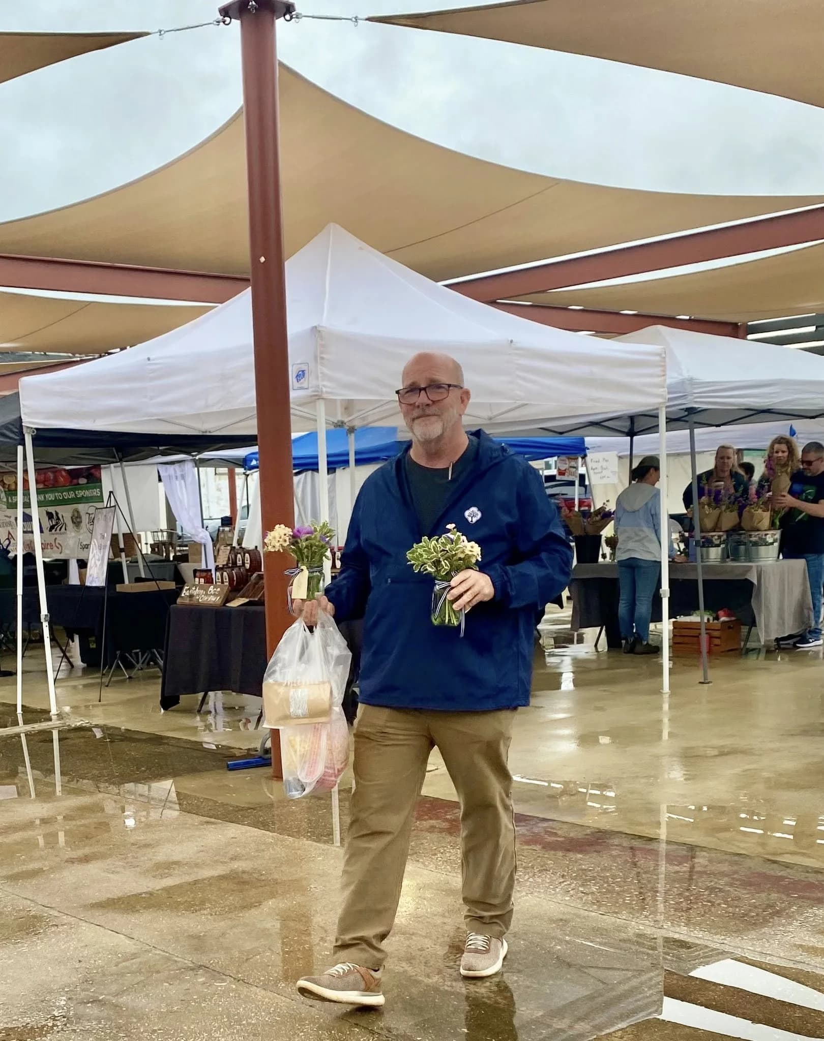 Jay Jenkins walking through the Anniston Farmers Market in the rain, carrying two bouquets