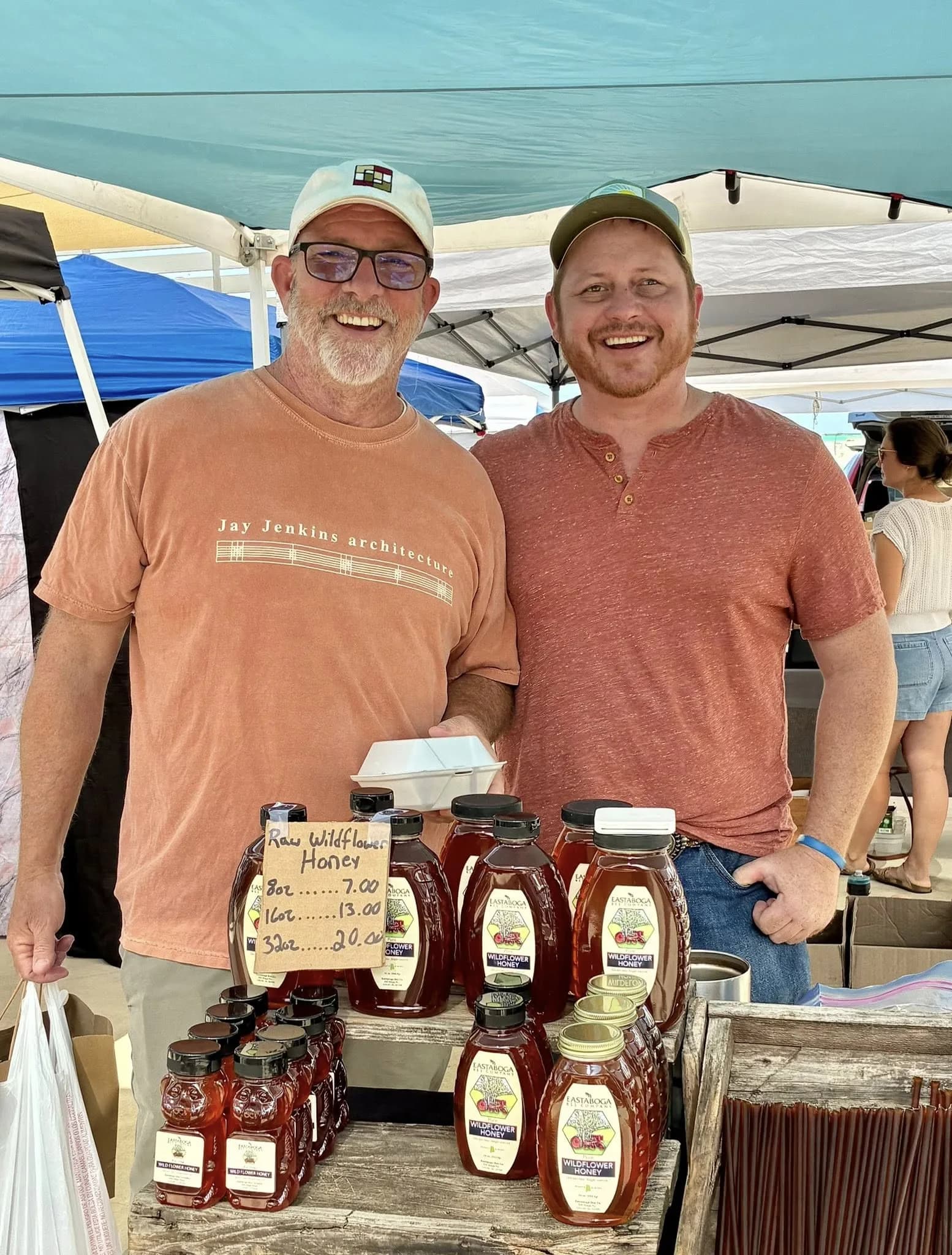 Jay Jenkins and Justin Hill at the Anniston Farmers Market honey booth, Jay wearing a Jay Jenkins architecture t-shirt
