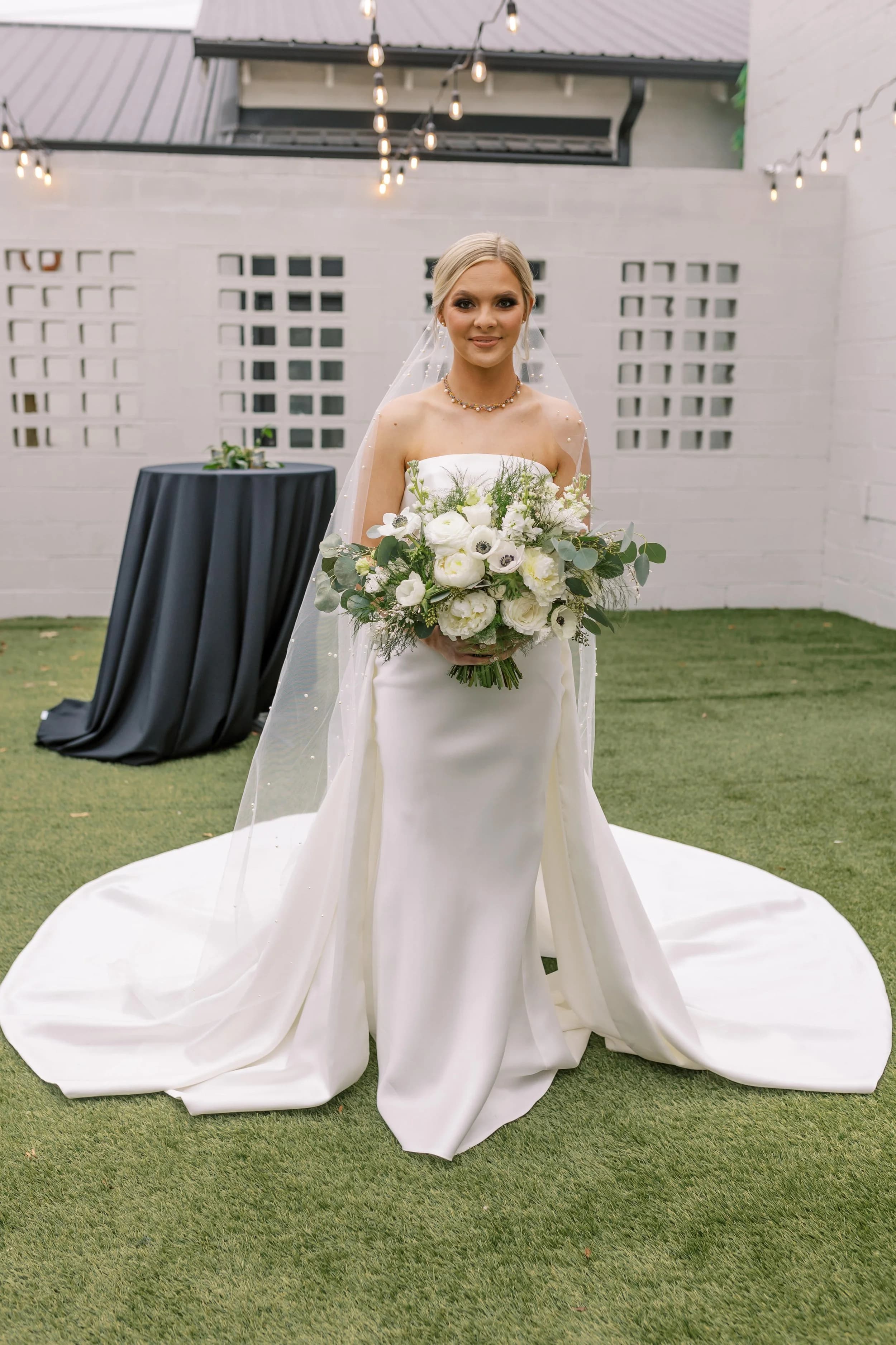 Sonny Jenkins in a white strapless gown on her wedding day, holding a bouquet of white ranunculus, anemones, and eucalyptus